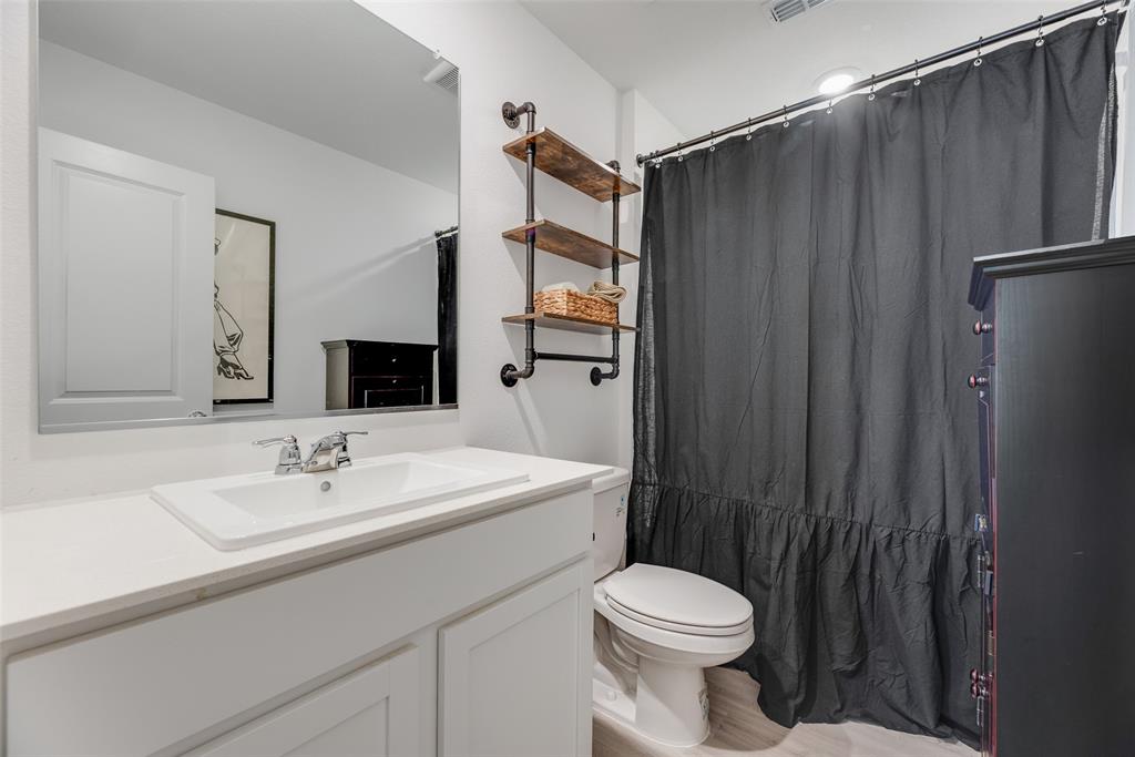 Bathroom featuring a white vanity with a rectangular drop-in sink, chrome hardware, a large frameless wall mirror, and industrial-style shelving with wood-finish tiered surfaces