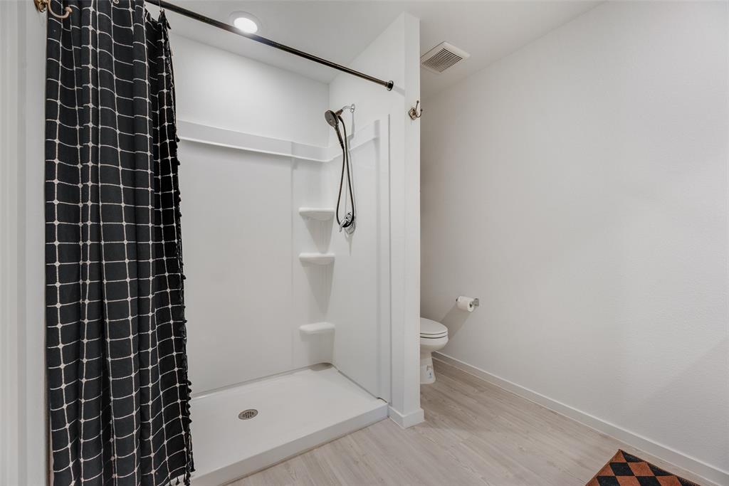 Bathroom featuring a white molded shower surround with integrated shelving, a handheld shower fixture, recessed lighting, and wood-finish flooring