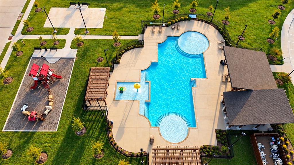 Recreational complex featuring an inground swimming pool, a splash pad with water features, a shaded pergola, a structured playground area, and a covered pavilion