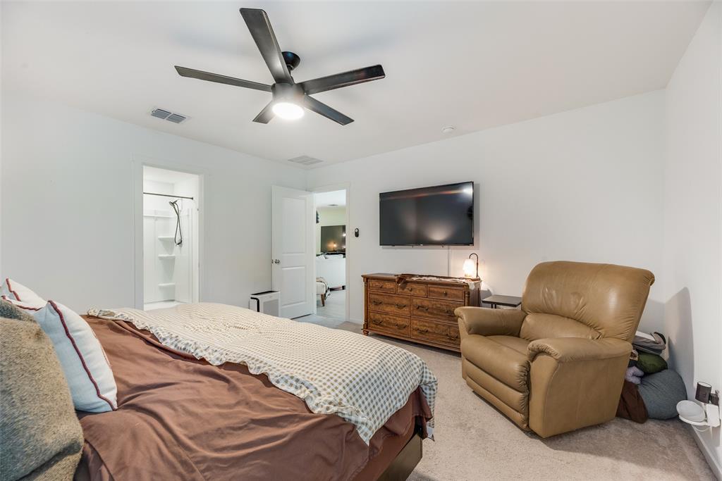 Spacious room featuring neutral carpeting, a central ceiling fan with integrated lighting, and a doorway entry to an en suite bathroom with a shower enclosure