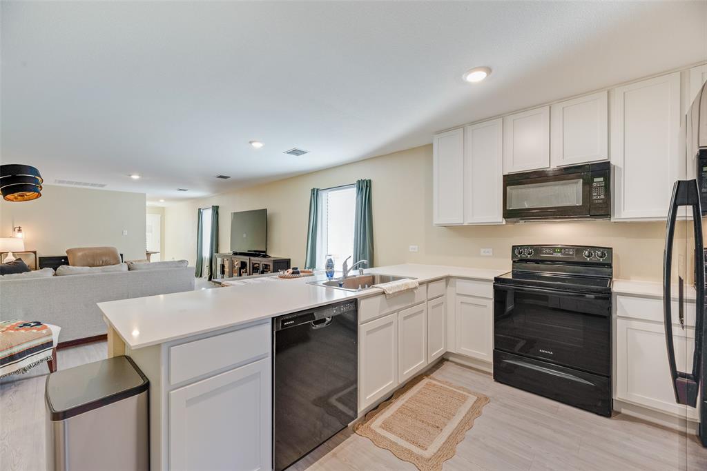 Kitchen featuring white cabinetry, solid-surface countertops, black appliances, a stainless steel sink, and light-tone wood-finish flooring