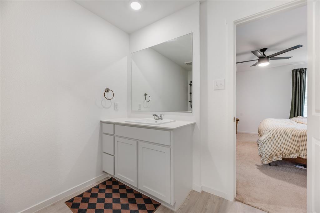 Bathroom vanity featuring white shaker-style cabinetry, a solid surface countertop with an integrated basin, a large wall-mounted mirror, and polished chrome hardware