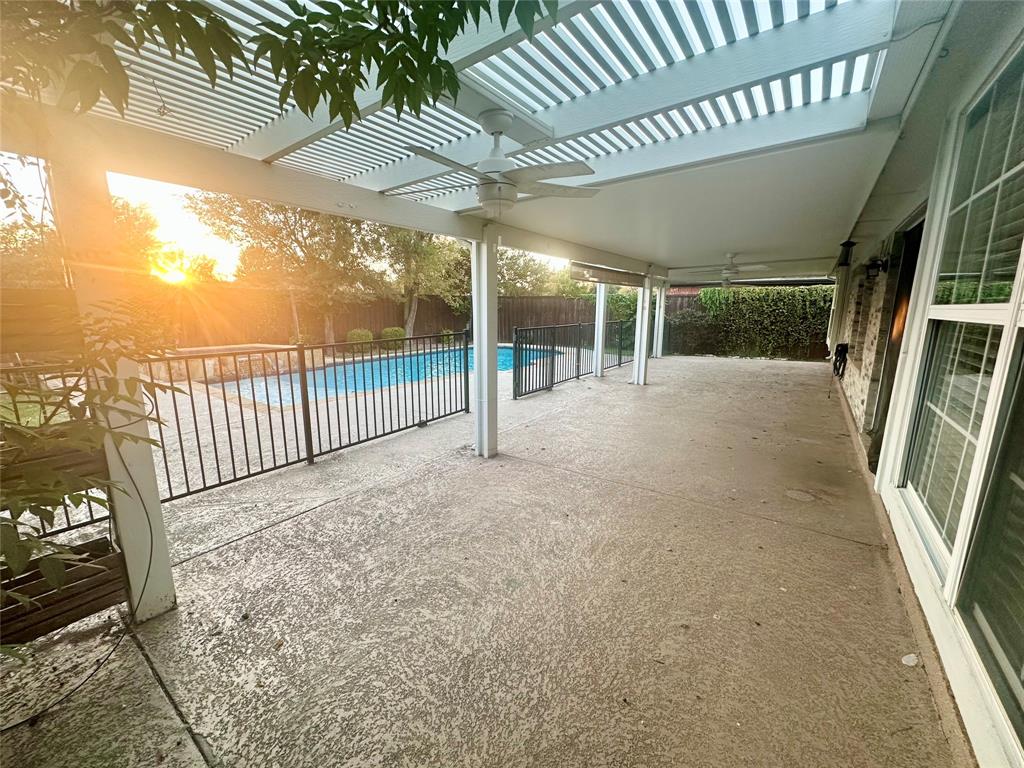 Covered concrete patio featuring a louvered pergola, ceiling fans, and a perimeter metal fence enclosing an in-ground pool