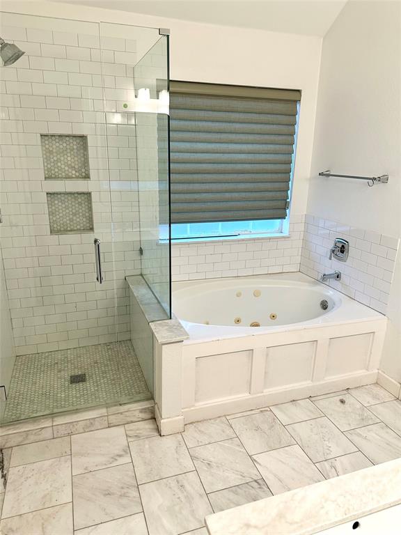 Walk-in shower with floor-to-ceiling subway tile, dual built-in wall niches, and a frameless glass enclosure, paired with a jetted soaking tub featuring custom white paneling and white tile surround