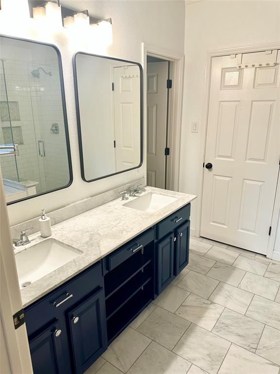 Dual vanity featuring navy blue shaker-style cabinetry, light-toned stone-finish countertops, undermount sinks, and rectangular mirrors with black frames, complemented by white tile flooring