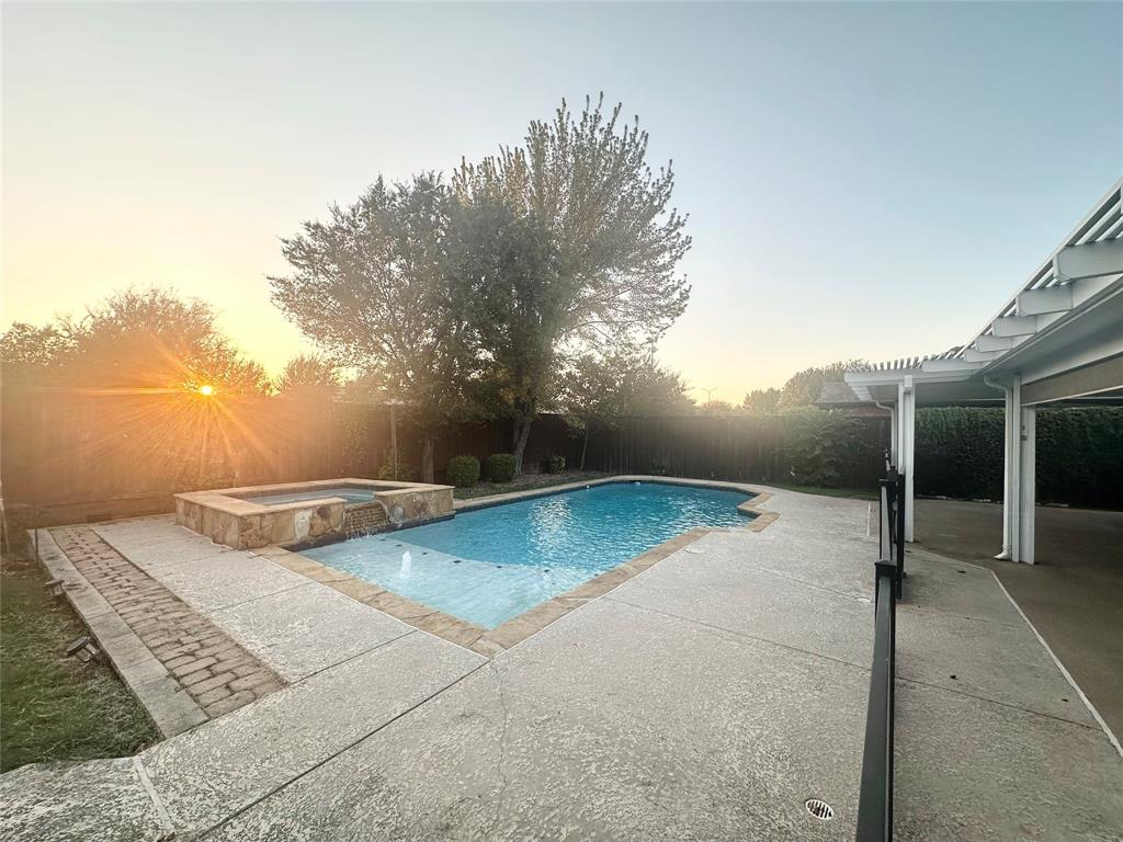 In-ground swimming pool with an integrated elevated stone spa, concrete patio surround, and a covered pergola
