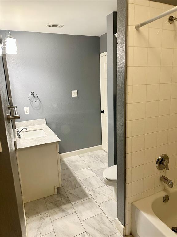 Bathroom featuring stone-finish countertop with integrated sink, vanity cabinet, tile flooring, and tiled shower enclosure with metal fixtures
