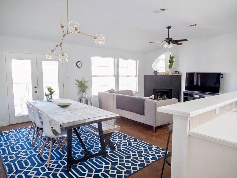 Open-concept space featuring wood-finish flooring, a contemporary multi-arm pendant light fixture, a black floor-to-ceiling fireplace surround, and double-glass paneled doors