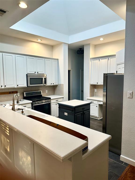 Kitchen featuring a central pyramid skylight, white shaker-style cabinetry, stainless steel appliances, a dark-toned center island, and solid-surface countertops