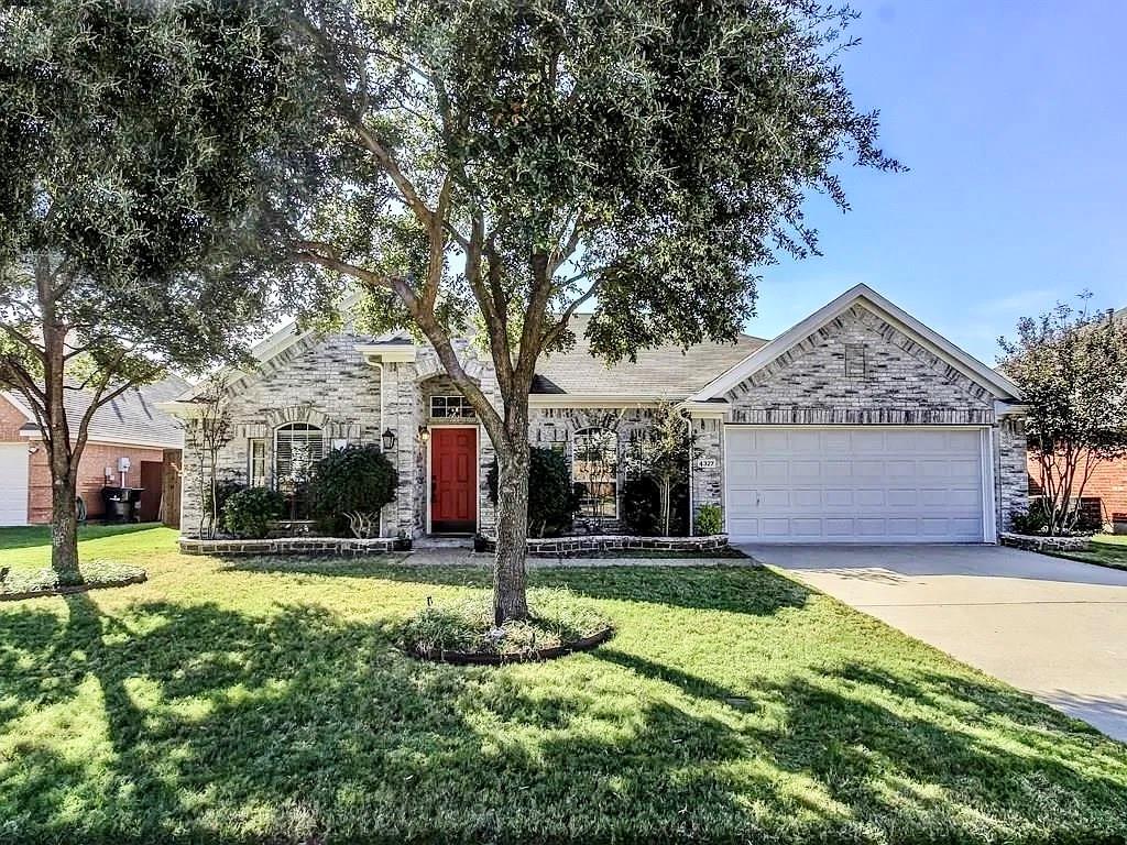 Single-story residence with a brick facade, arched window detailing, front-facing two-car garage, mature landscaping, and an arched entryway