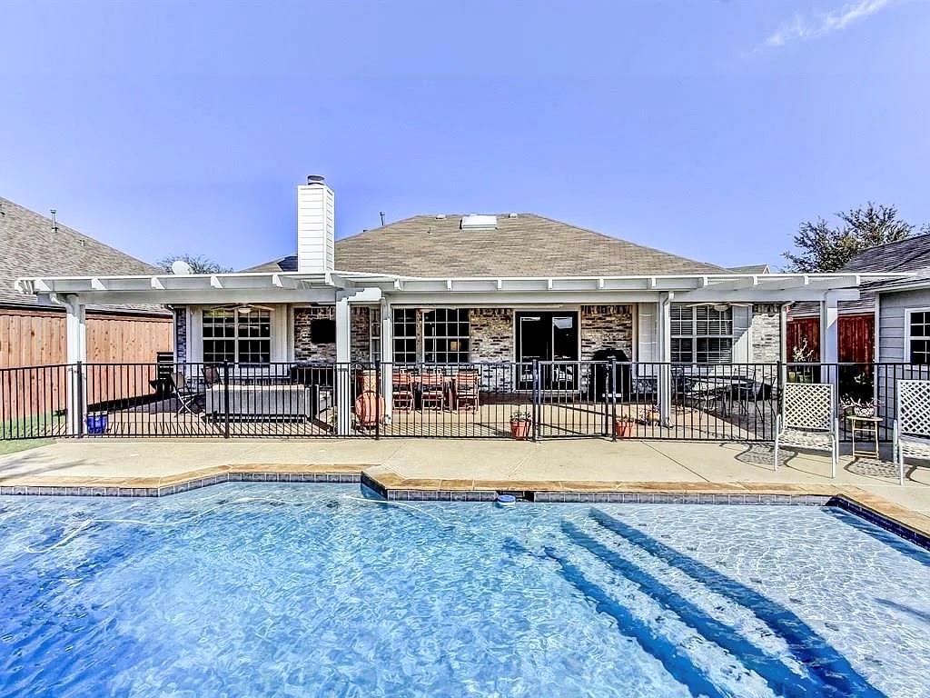 In-ground swimming pool with steps, concrete patio, covered pergola, brick exterior, and metal fencing