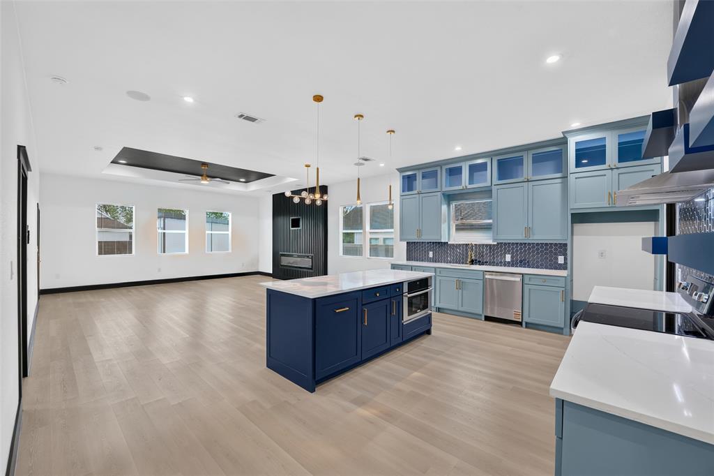 Kitchen featuring custom cabinetry, a central island with quartz countertops, wood-finish flooring, a geometric tile backsplash, and a recessed ceiling tray Kitchen featuring custom cabinetry, a central island with quartz countertops, wood-finish flooring, a geometric tile backsplash, and a recessed ceiling tray