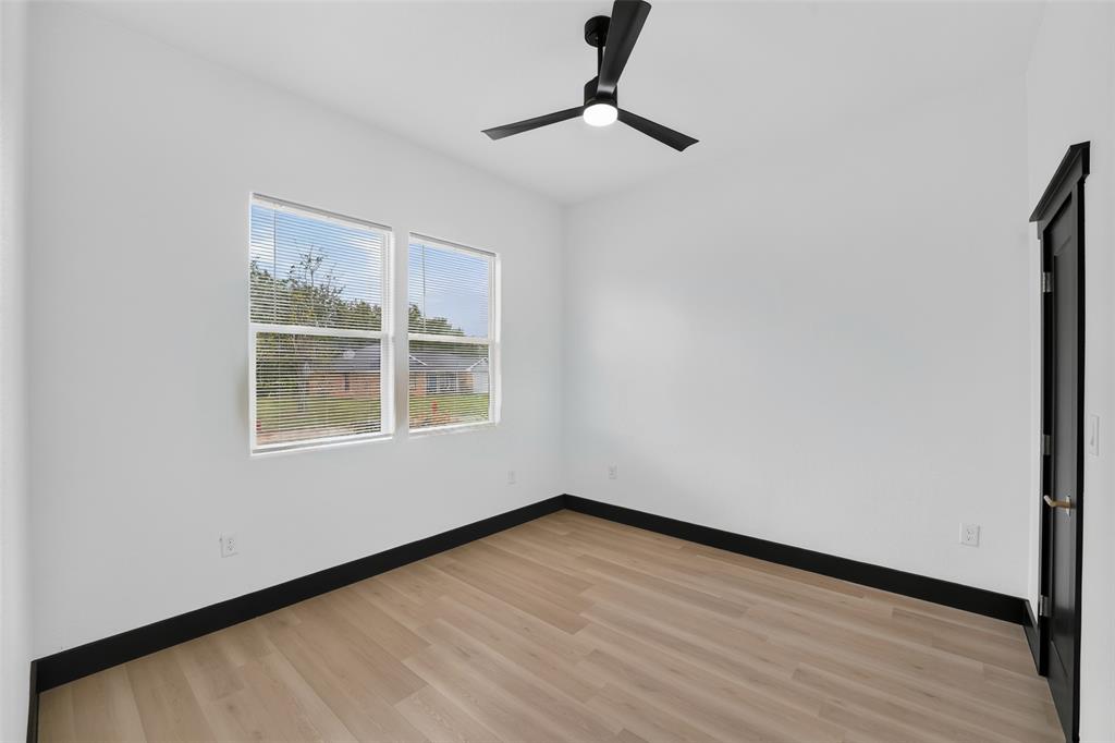 Neutral-toned room featuring wood-finish flooring, matte black trim, a minimalist ceiling fan with integrated lighting, and dual windows