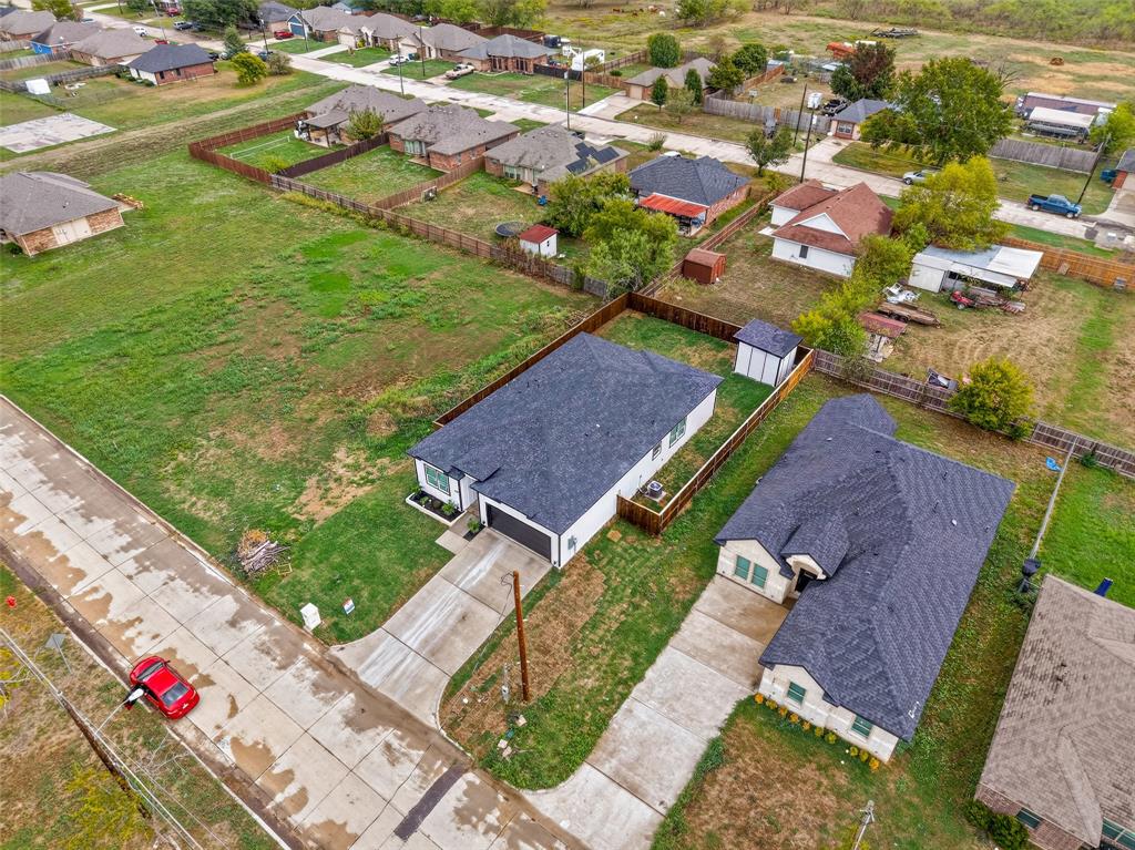 Aerial perspective of a detached single-story residence featuring an asphalt shingle roof, concrete driveway, attached garage, and a fenced yard with a detached storage structure