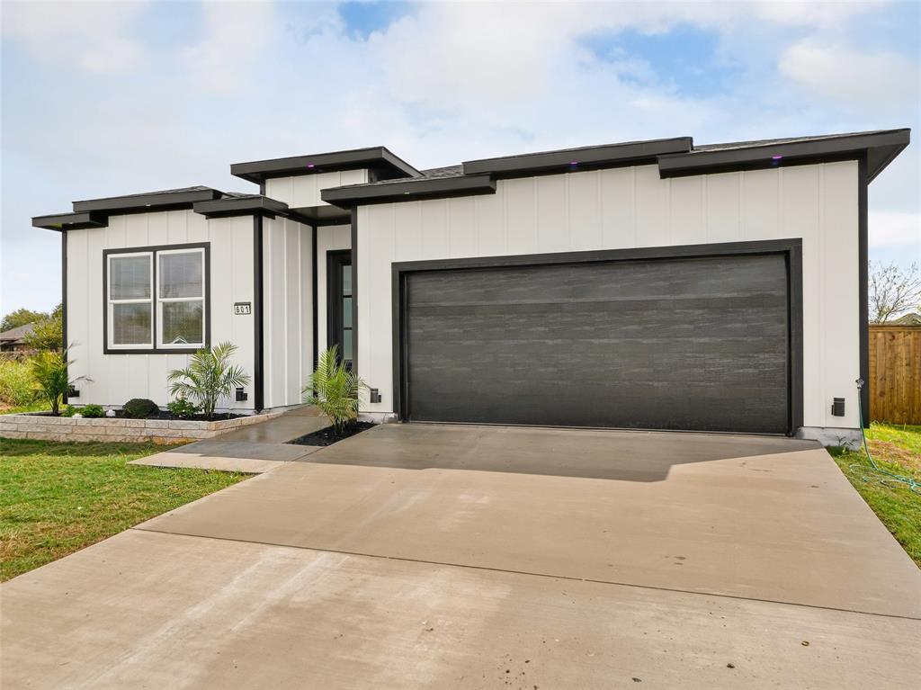 Modern exterior featuring vertical board-and-batten siding, a multi-level flat roofline, a dark-finish garage door, and a stone-trimmed front garden bed