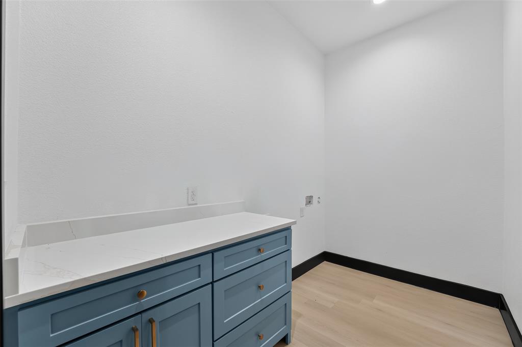 Blue cabinetry with metal hardware, solid-surface countertop with integrated backsplash, and light wood-finish flooring