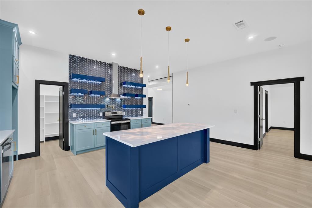 Kitchen featuring a central island with a solid surface countertop, honeycomb-patterned tile backsplash, integrated floating shelves with recessed lighting, and wood-finish flooring Kitchen featuring a central island with a solid surface countertop, honeycomb-patterned tile backsplash, integrated floating shelves with recessed lighting, and wood-finish flooring