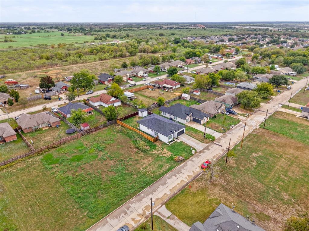 Aerial perspective of a residential lot featuring a single-story structure with a dark shingle roof, paved driveway, enclosed rear yard, and proximity to open green space