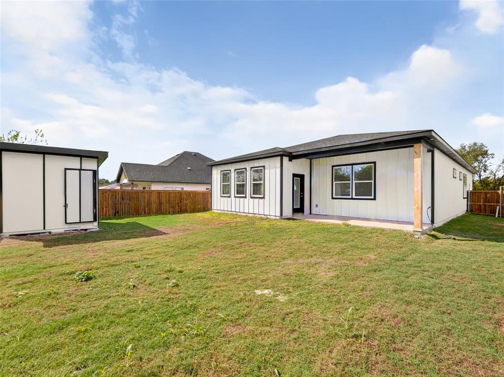 Exterior featuring vertical board-and-batten siding, a covered patio, a detached storage structure, and a wood-slat perimeter fence