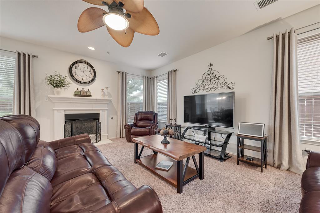 Living area featuring a fireplace with a white mantel, high ceilings, multiple windows with neutral drapery, and a multi-blade ceiling fan Living area featuring a fireplace with a white mantel, high ceilings, multiple windows with neutral drapery, and a multi-blade ceiling fan