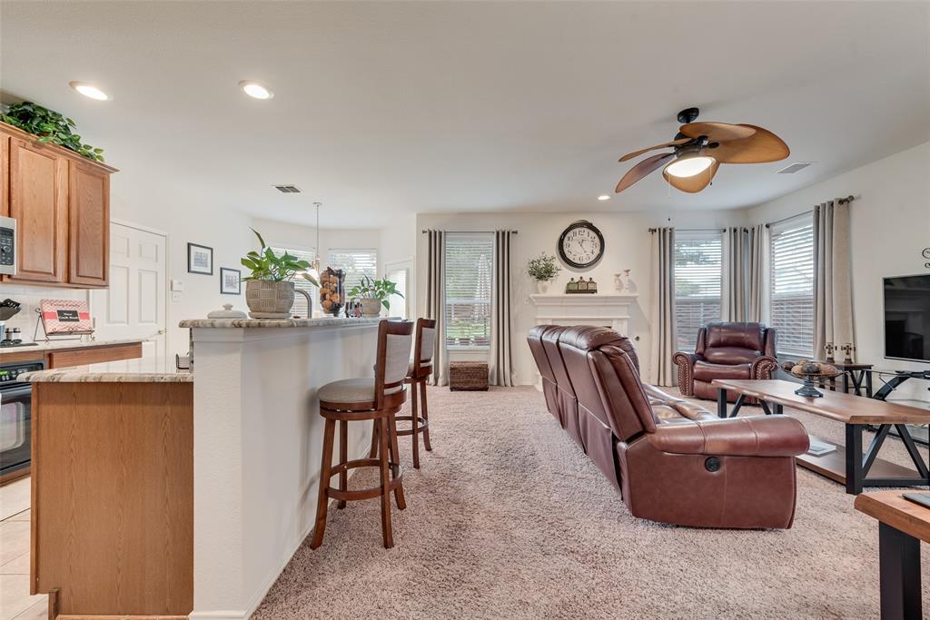 Open-concept interior featuring wood cabinetry, stone-surfaced kitchen island, tile-surround fireplace, and decorative ceiling fan with integrated lighting Open-concept interior featuring wood cabinetry, stone-surfaced kitchen island, tile-surround fireplace, and decorative ceiling fan with integrated lighting