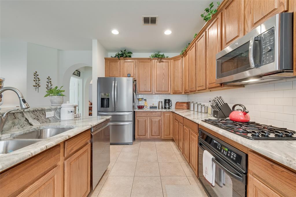 Galley kitchen featuring warm wood cabinetry, stainless steel appliances including a French-door refrigerator and gas cooktop, white subway tile backsplash, and quartz countertops with an undermount sink Galley kitchen featuring warm wood cabinetry, stainless steel appliances including a French-door refrigerator and gas cooktop, white subway tile backsplash, and quartz countertops with an undermount sink