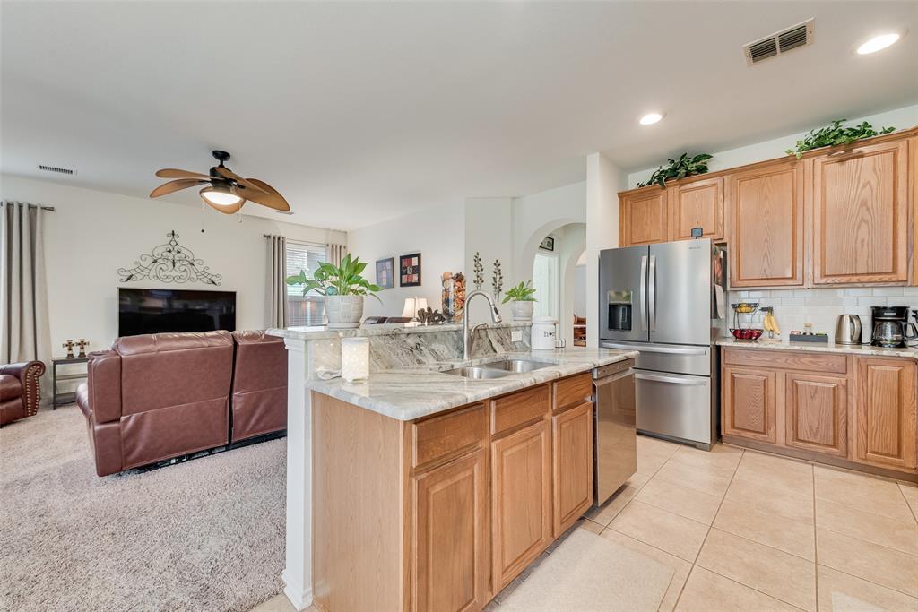 Kitchen featuring wood cabinetry, stone countertops, a stainless steel refrigerator, tile flooring, and a ceiling fan