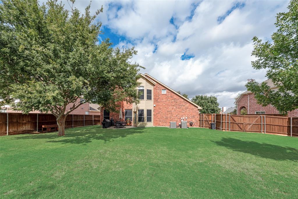 Fenced backyard featuring a manicured lawn, mature trees, and a concrete patio