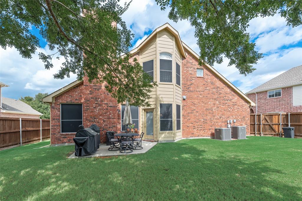 Brick exterior featuring a multi-story rear elevation, expansive lawn, concrete patio, and wooden perimeter fencing