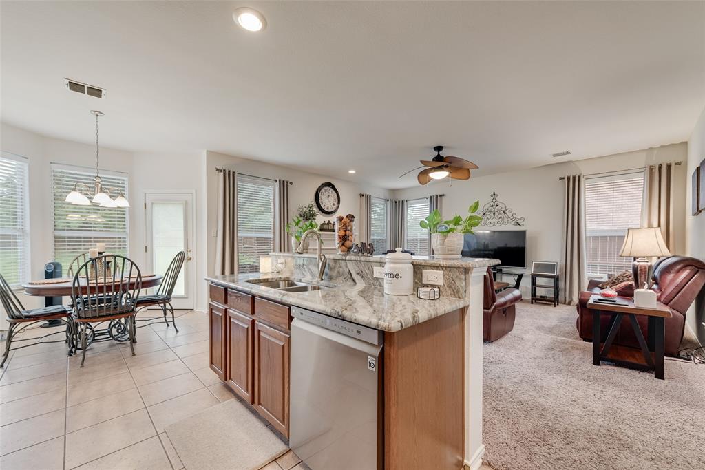 Kitchen island with stone countertop, stainless steel dishwasher, wood-finish cabinetry, tile flooring, and ceiling fan Kitchen island with stone countertop, stainless steel dishwasher, wood-finish cabinetry, tile flooring, and ceiling fan