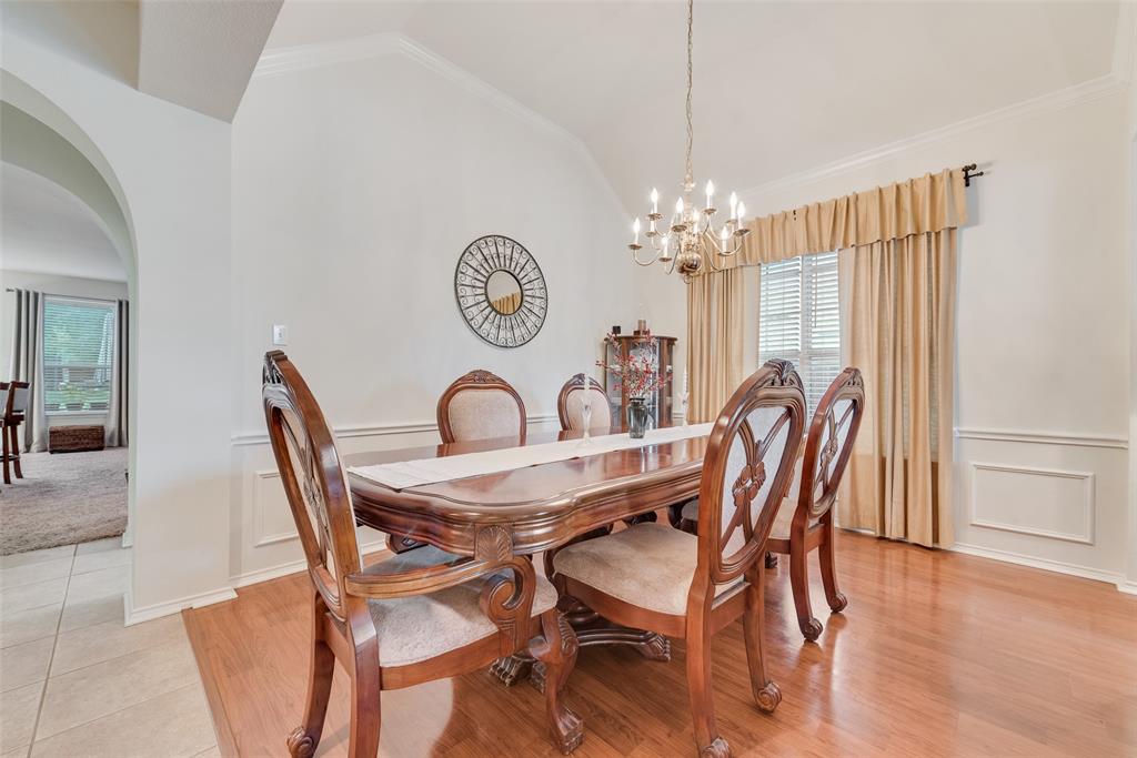Dining area featuring vaulted ceilings, wood-finish flooring, decorative wall molding, and a multi-arm chandelier