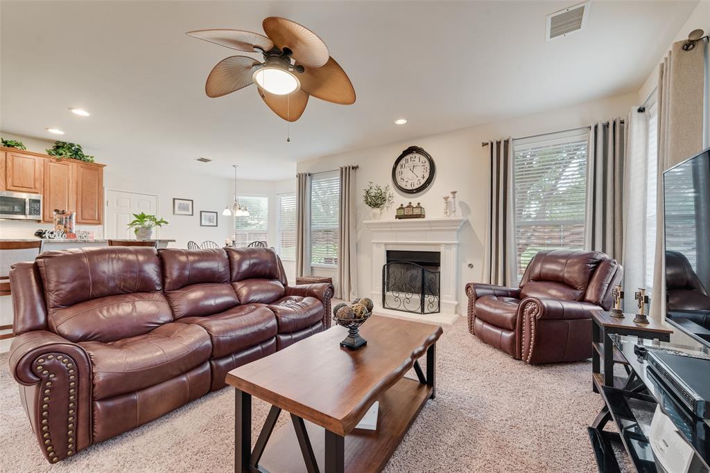 Living area featuring a fireplace with a white mantel, ceiling fan with palm-style blades, recessed lighting, and multiple windows Living area featuring a fireplace with a white mantel, ceiling fan with palm-style blades, recessed lighting, and multiple windows
