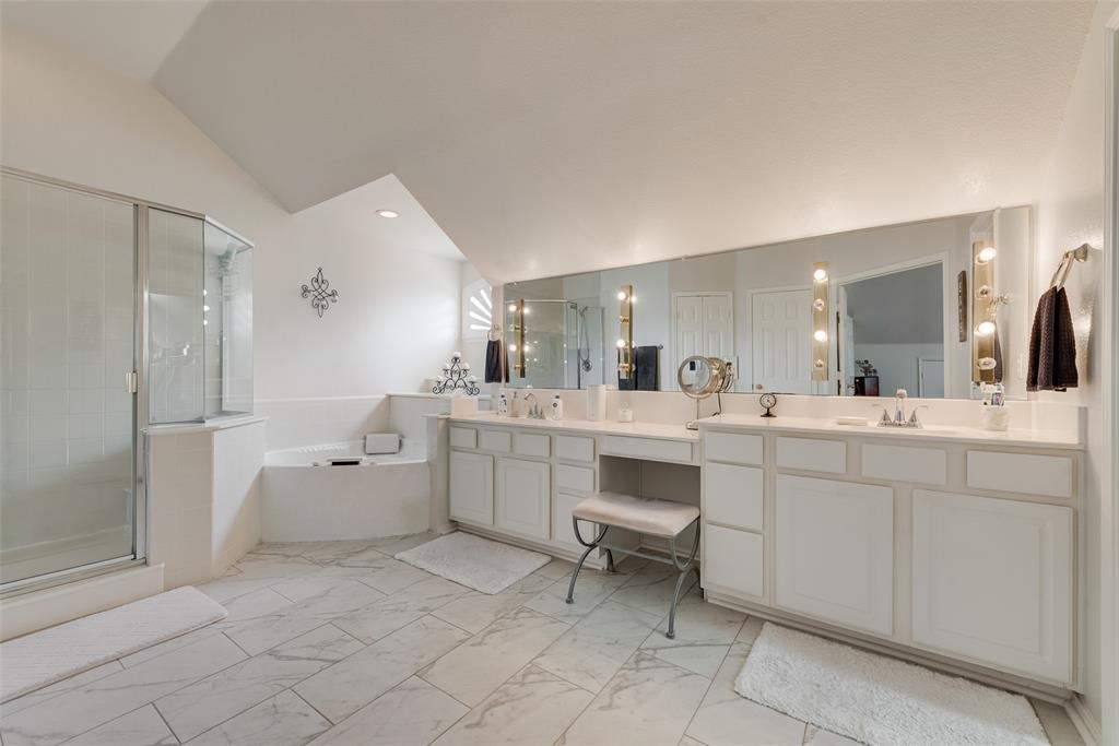 Bathroom featuring tile flooring, a dual-sink vanity with built-in cabinetry, an integrated makeup vanity, a corner soaking tub, and a glass-enclosed shower