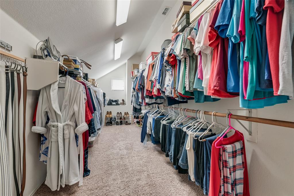 Walk-in closet featuring extensive built-in hanging rods, overhead shelving, neutral carpeted flooring, and linear fluorescent lighting