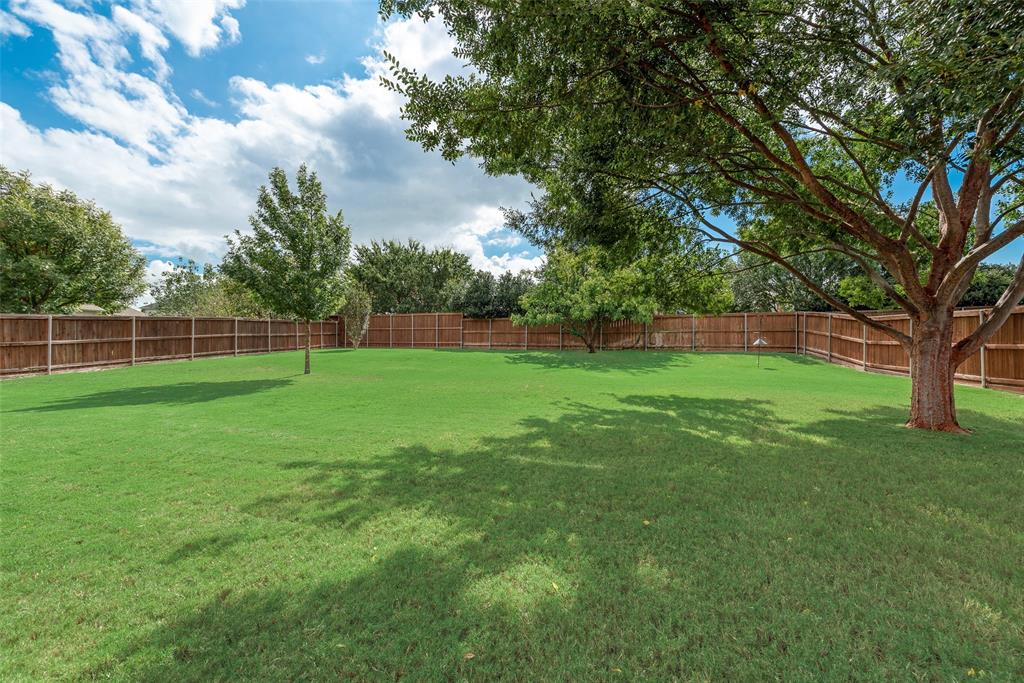 Expansive backyard featuring a level lawn, mature trees, and a full-perimeter wood privacy fence