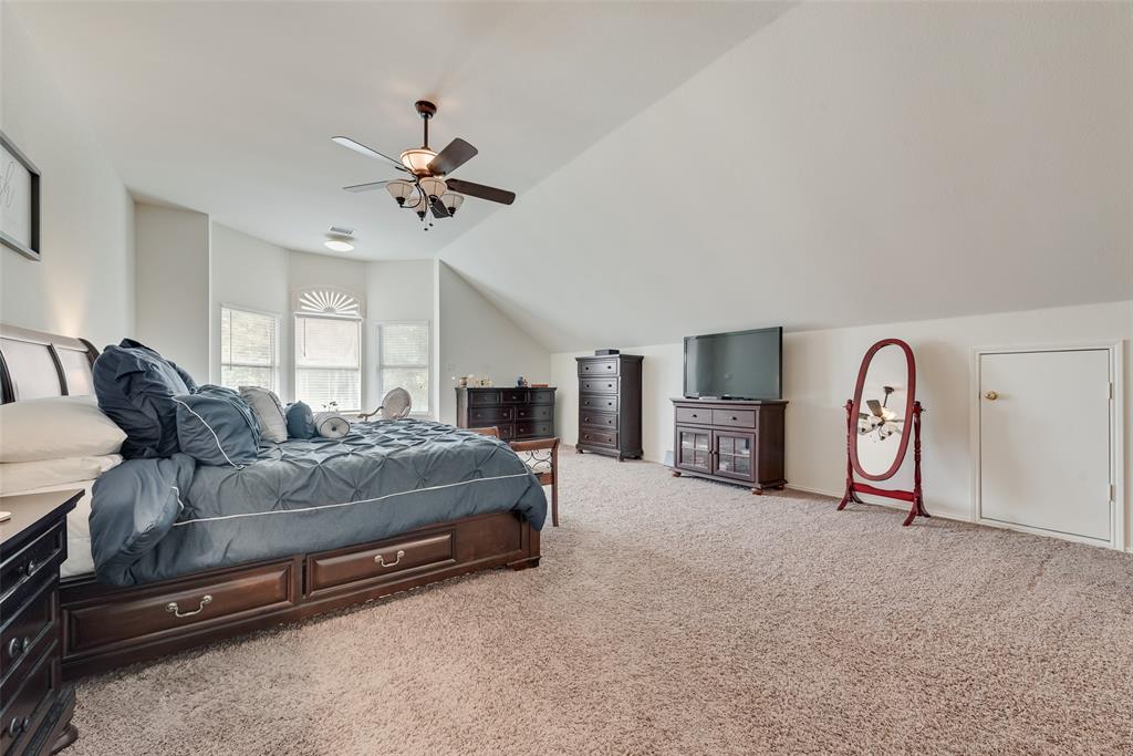 Vaulted ceilings featuring a multi-pane bay window, carpeted flooring, a ceiling fan with integrated lighting, and an access door to attic storage