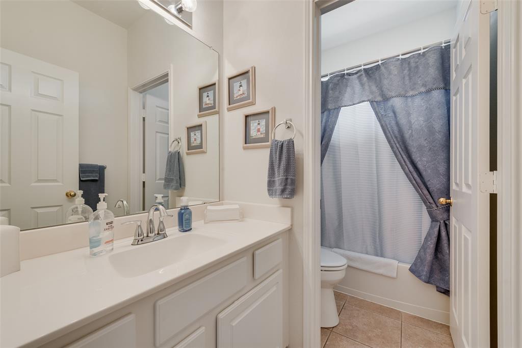 Bathroom featuring a solid-surface countertop with an integrated sink, polished chrome faucet, expansive wall-to-wall mirror, built-in cabinetry, and ceramic tile flooring