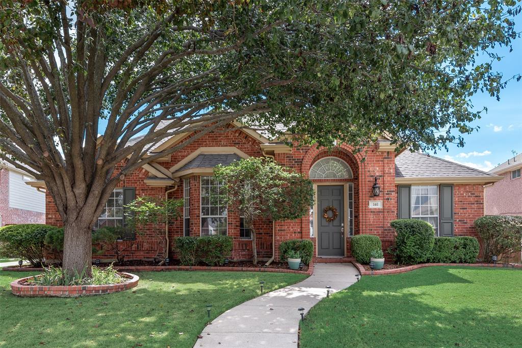 Brick exterior featuring an arched entryway, a bay window, a manicured lawn, and a mature tree with a circular brick planter Brick exterior featuring an arched entryway, a bay window, a manicured lawn, and a mature tree with a circular brick planter
