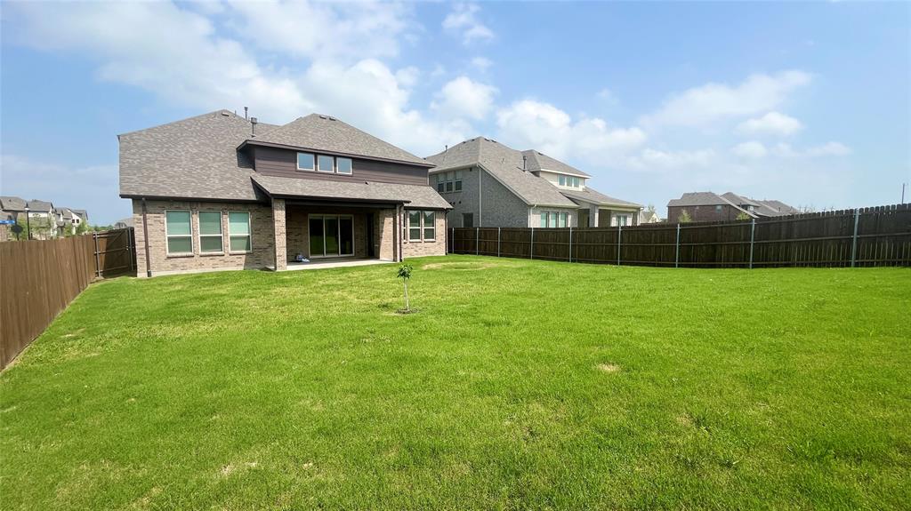 Spacious backyard with a grass lawn, covered patio, masonry exterior, and perimeter wood fencing