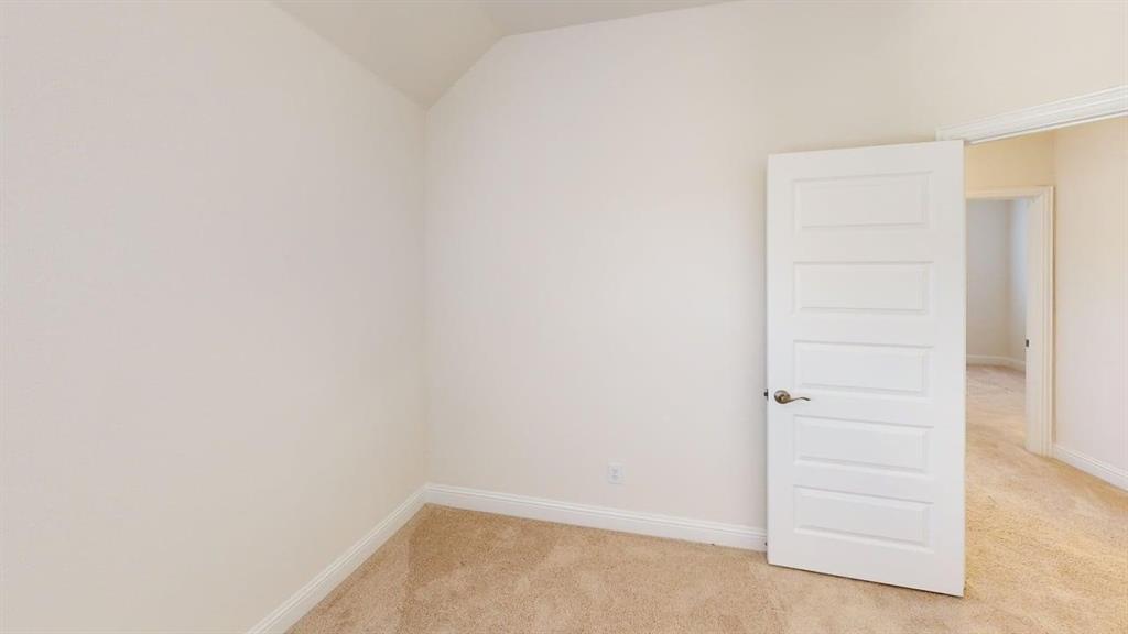 Neutral-toned room featuring a vaulted ceiling, wall-to-wall carpeting, and a five-panel interior door with a brushed metallic lever handle