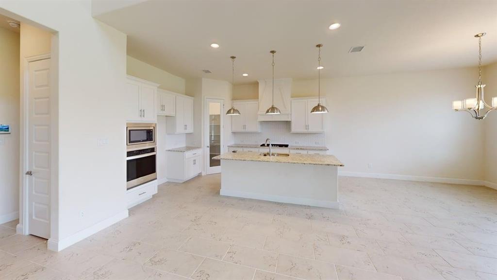 Kitchen featuring white cabinetry, stone-surface countertops, built-in stainless steel double oven and microwave, stone-finish tile flooring, and three pendant lights over a central island