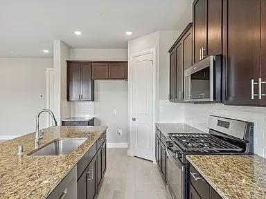 Kitchen featuring dark wood cabinetry, stone countertops, stainless steel gas range, built-in microwave, and an island with a stainless steel undermount sink