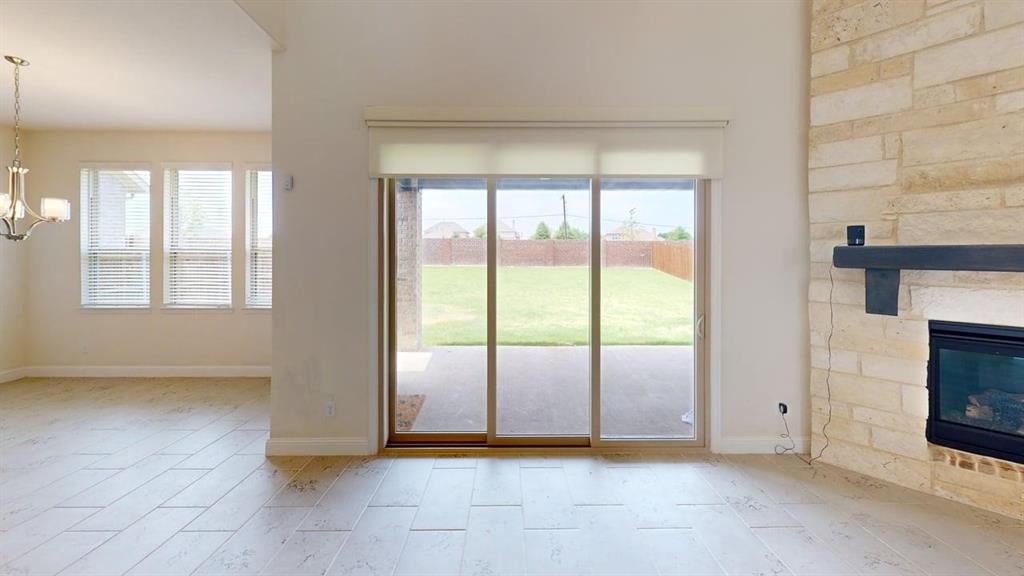 High-ceilinged room featuring a floor-to-ceiling stone fireplace, wood-finish tile flooring, sliding glass door, and multi-pane windows