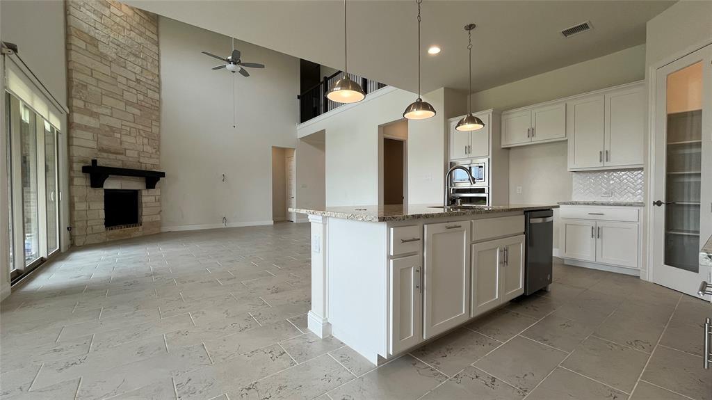 Double-height ceiling with stone-faced fireplace, kitchen island featuring stone countertops, white cabinetry, herringbone-patterned tile backsplash, and tile flooring