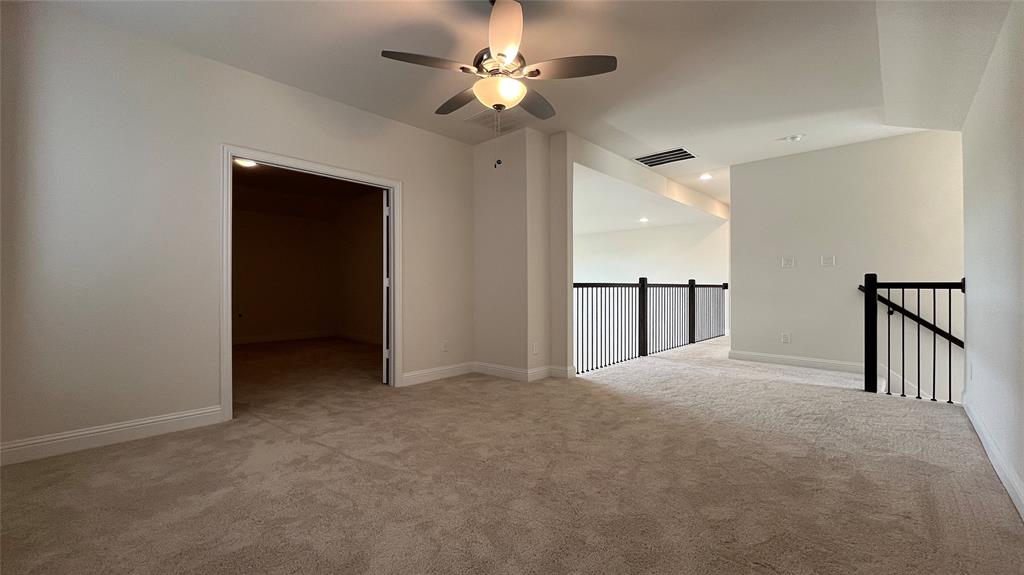 Neutral-toned interior space featuring carpeting, a ceiling fan with integrated lighting, recessed lighting, and a metal balustrade staircase railing