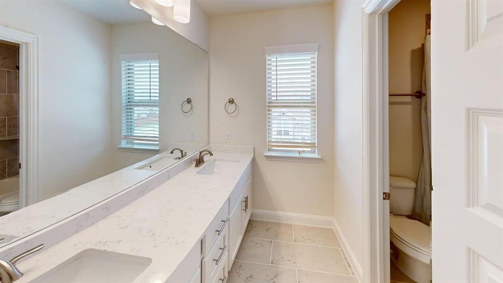 Dual-sink vanity with white stone-finish countertop, full-width wall mirror, tile flooring, and dedicated enclosed water closet