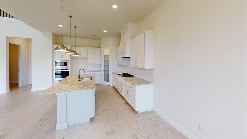 Kitchen featuring white cabinetry, stone-surface countertops, center island with undermount sink, built-in double wall oven, and pendant lighting
