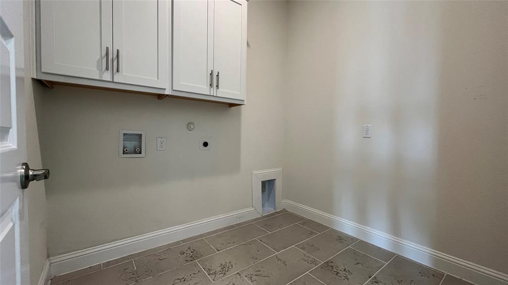 Utility room featuring white shaker-style wall cabinets with brushed nickel hardware, neutral-toned tile flooring, and dedicated hookups for laundry appliances