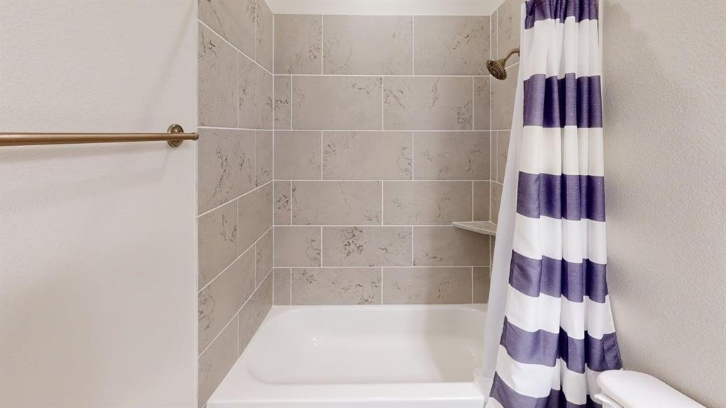 Full-height shower surround featuring large-format neutral tile with decorative inlay, integrated corner shelf, and metallic finish shower head and wall-mounted towel bar