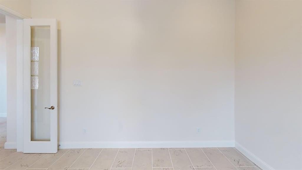 Neutral wall finish paired with light-toned ceramic tile flooring and a white French door featuring decorative glass panes